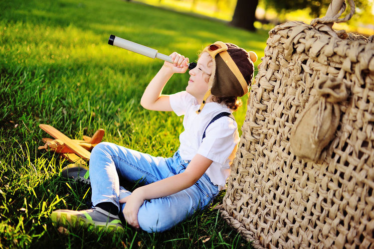 Small boy  sits on the grass leaning on a balloon basket against the background of trees