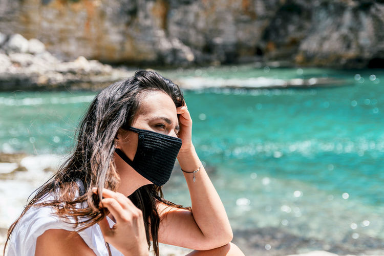 Portrait of a young woman wearing black protective mask on beach in summer. tourist, corona, covid.