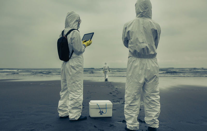 Rear view of man and woman with first aid kit standing on beach
