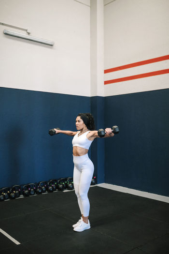 Sportswoman with arms raised exercising dumbbells in gym