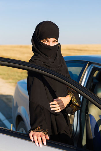 Portrait of woman in hijab standing by car outdoors