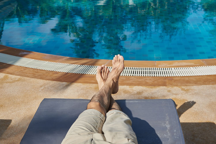 Low section of man relaxing by swimming pool