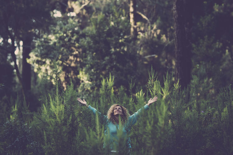 Woman with arms raised standing amidst plants in forest