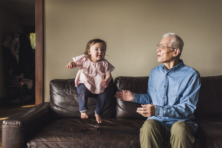 Granddaughter jumping on couch in living room with grandfather