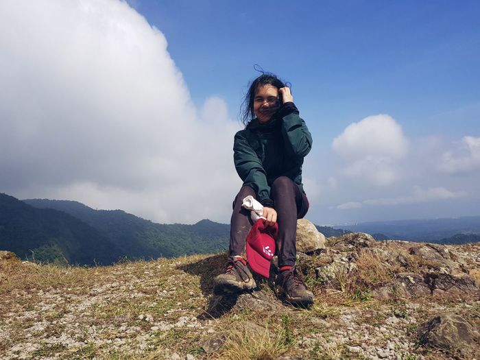 Full length of young woman sitting on mountain against sky