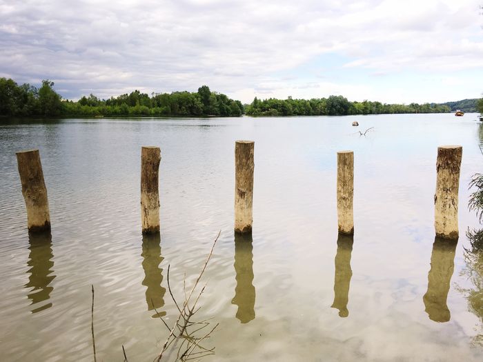 Wooden posts in lake against cloudy sky