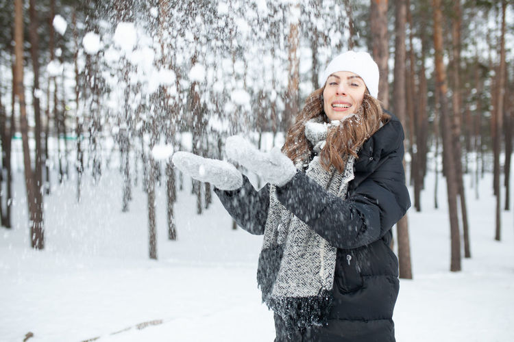 Portrait of happy woman playing with snow in forest