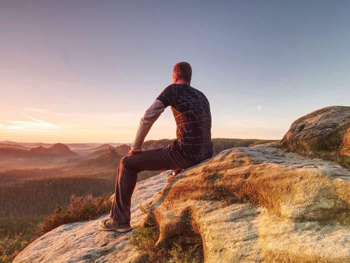 Flare. strong lens defect reflections. man in sportswear is sitting on cliff's edge above valley