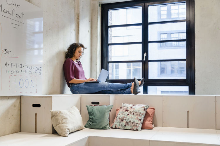 Female entrepreneur using laptop while sitting with legs crossed at ankle in office