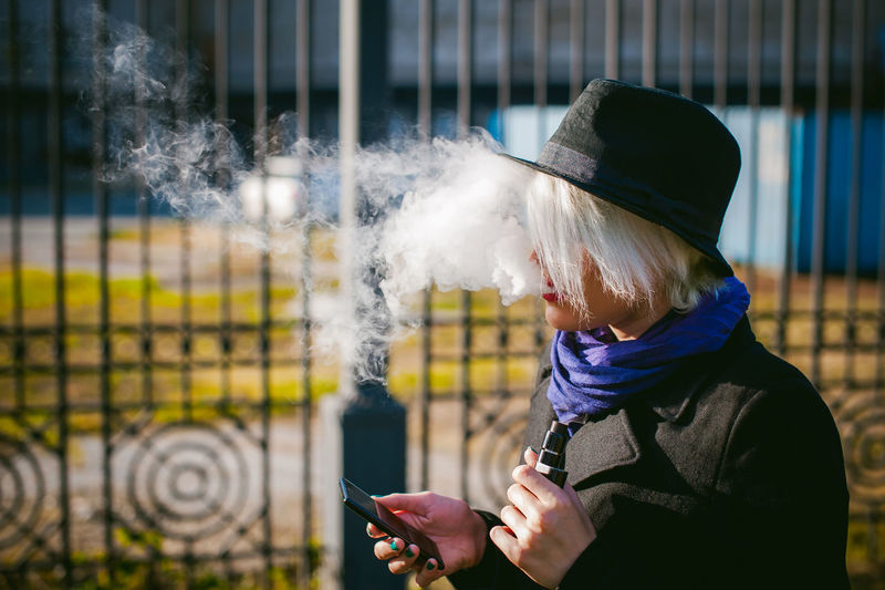 Side view of woman using mobile phone while smoking