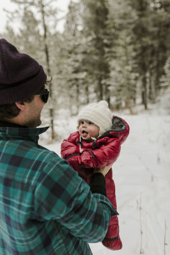 Side view of father carrying cute daughter while standing in forest during winter