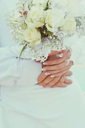 Cropped hands of bride and groom holding hands with bouquet