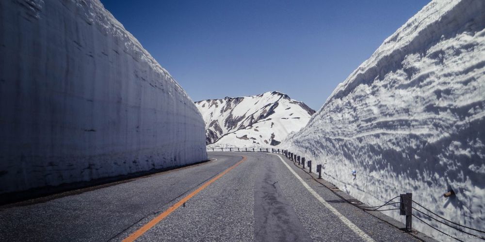 Road amidst snowcapped mountains against clear blue sky