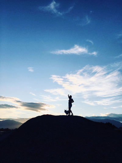 Low angle view of silhouette woman standing on hill against sky during sunset