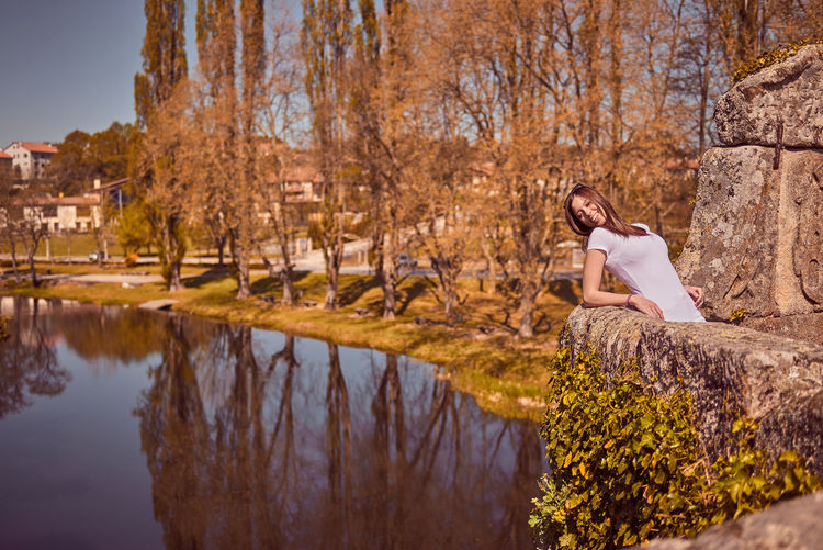 Smiling woman leaning on retaining wall over lake during autumn