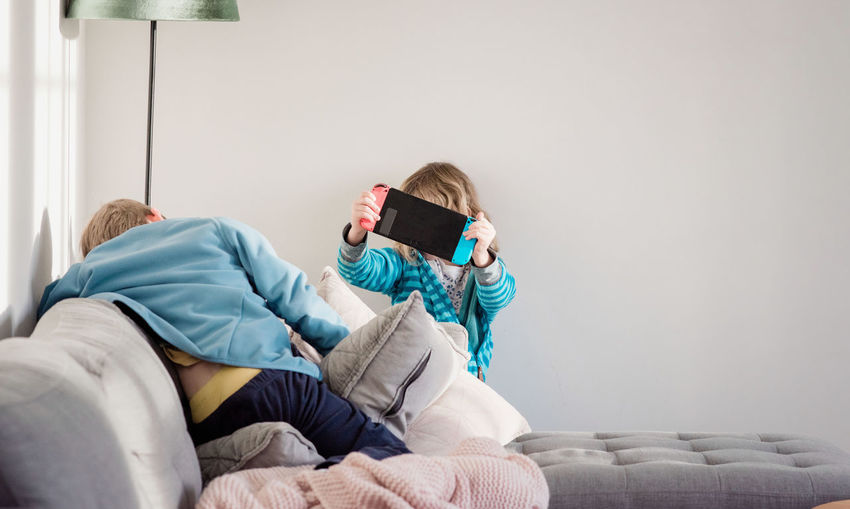 Brother and sister playing nintendo switch at home on the sofa