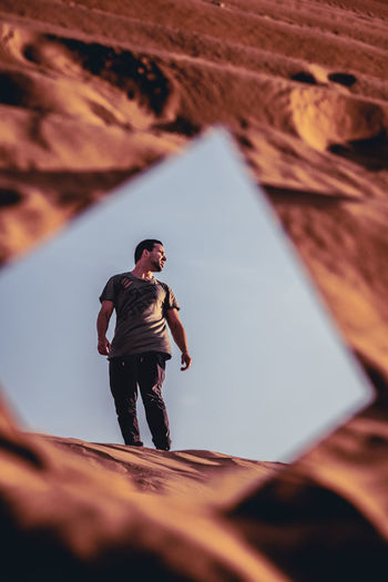 Reflection of man standing on sand in mirror