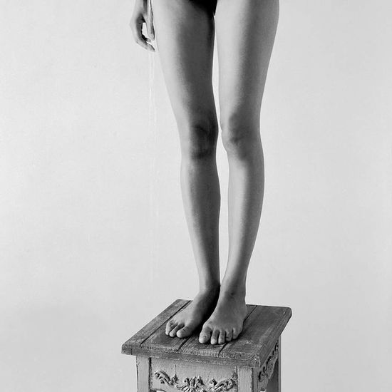 Low section of naked woman standing on wooden stool against white background