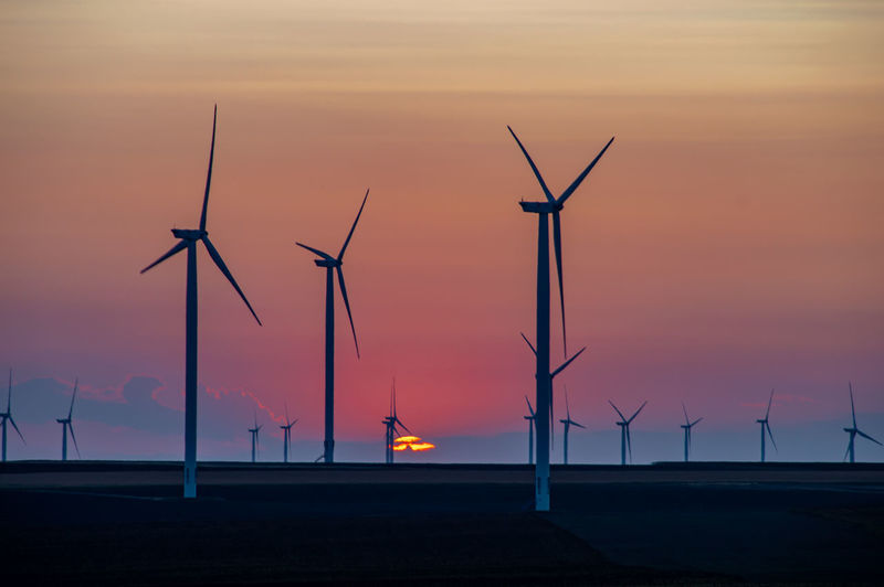 Silhouette wind turbine against sky during sunset