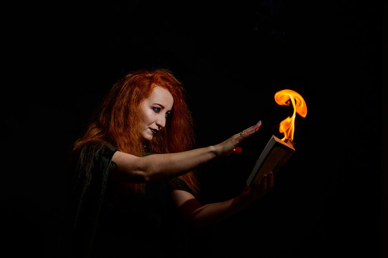 Woman holding burning book against black background