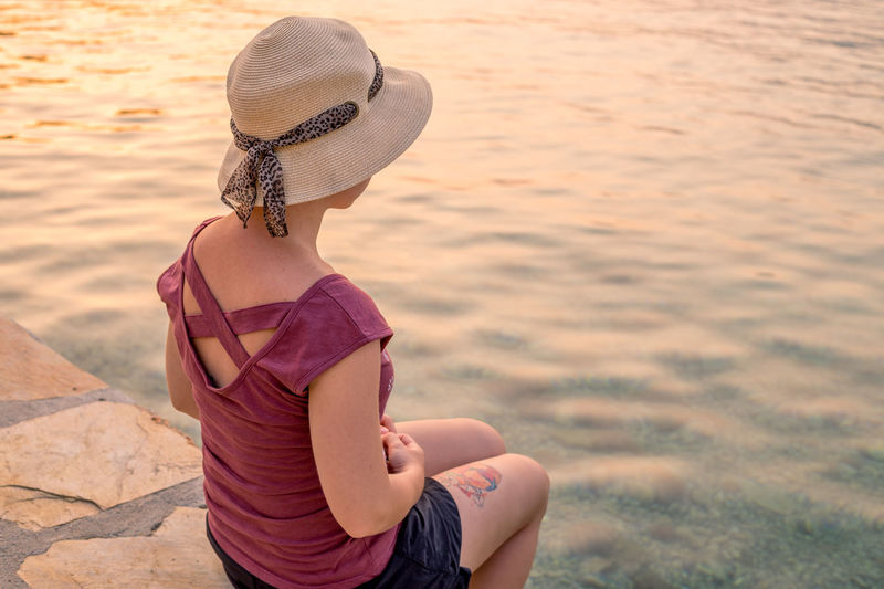 High angle view of girl in hat sitting by river during sunset