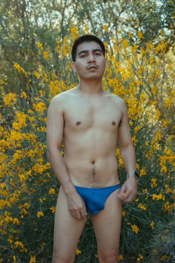Portrait of shirtless man standing amidst yellow flowering plants on field