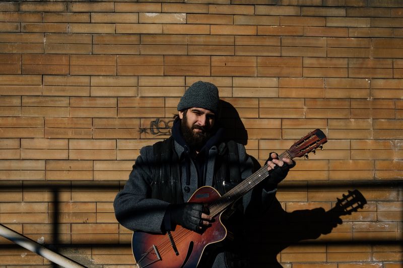 Portrait of man playing guitar while standing against brick wall