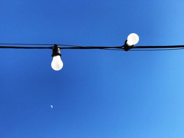 Low angle view of light bulbs against clear blue sky