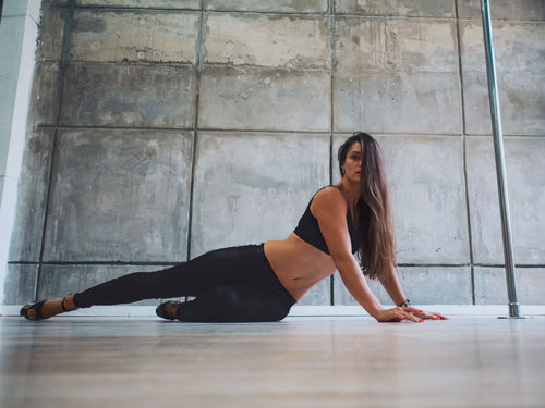 Full length portrait of sensuous pole dancer on floor in studio