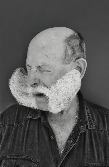Close-up of bearded man making face against gray background