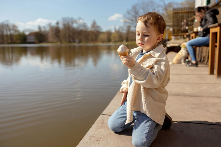 Little adorable boy sitting outdoors and eating ice cream. lake, water and sunny weather.