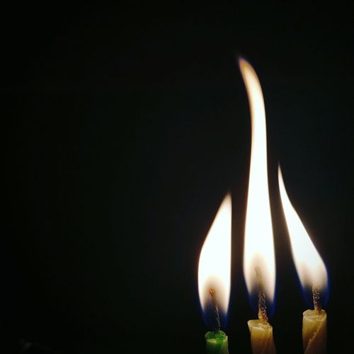 Close-up of three candles burning against black background