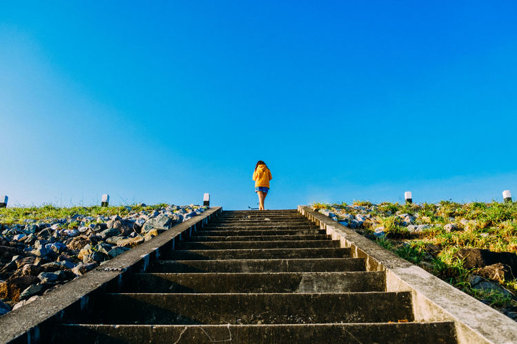 Rear view of woman standing on steps against clear blue sky