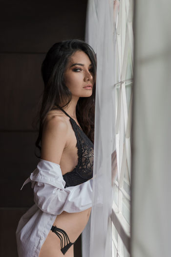 Seductive woman wearing lingerie and unbuttoned shirt by window