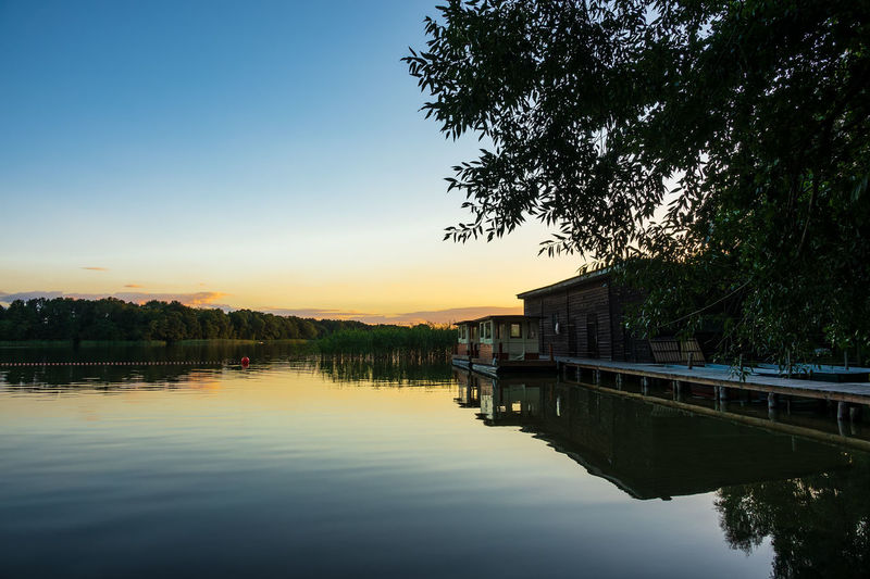House by lake against sky during sunset