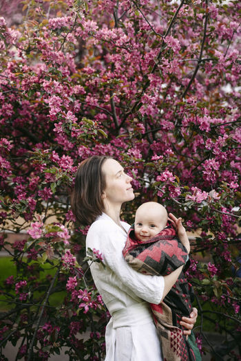Woman with cute baby boy standing in front of apple blossom tree