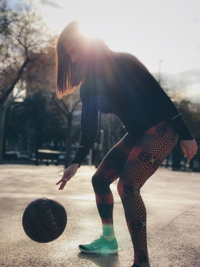 Woman playing basketball at court during sunny day