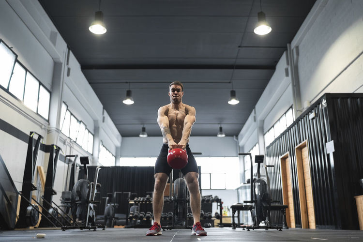 Male athlete picking up kettlebell while standing in exercise room