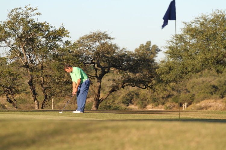 Side view of mature man playing golf on grassy field against trees