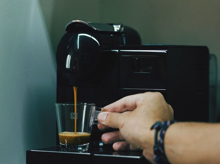 Cropped hand of man holding cup by espresso maker