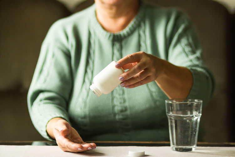 Elderly woman hands holds plastic bottle with pills and ready to take supplement with glass of water