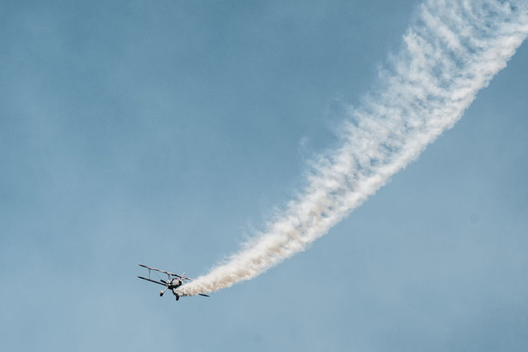 Low angle view of military airplane performing airshow against blue sky