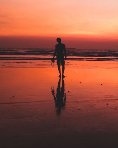 Silhouette person standing on beach against sky during sunset