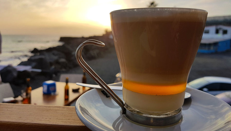 Close-up of coffee cup on table against sea during sunset