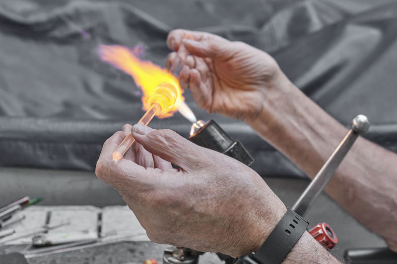 Hands of mature glassblower.process of artistic glass processing by burner flame