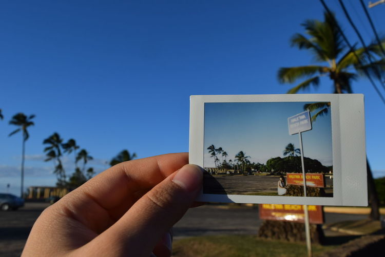 Cropped hand holding instant print transfer against blue sky