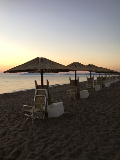 Parasols and chairs arranged at beach against sky during sunset
