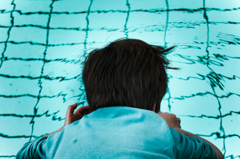 Rear view of boy dipping head in swimming pool