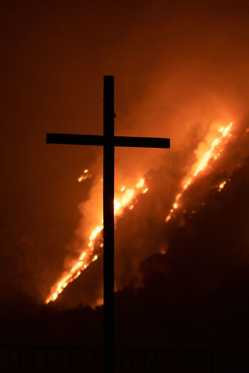 Low angle view of silhouette cross against fire at night