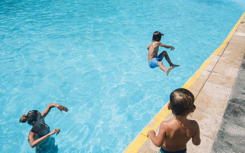 A woman and kid look at a boy jumping into a pool